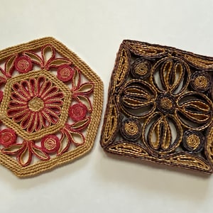 May include: Two woven trivets, one in a hexagonal shape with red and brown accents, and the other in a square shape with brown and gold accents.