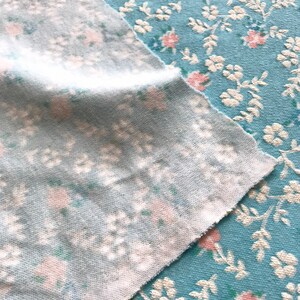 May include: Two pieces of light blue fabric with a white and pink floral pattern. The fabric is textured and has a soft, fuzzy feel.