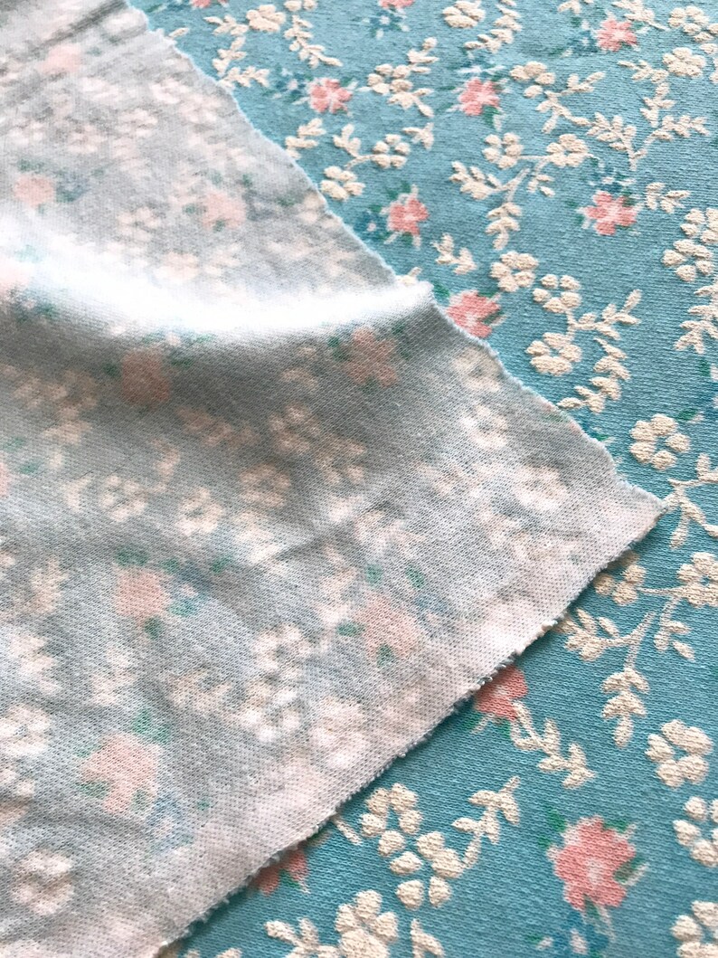May include: Two pieces of light blue fabric with a white and pink floral pattern. The fabric is textured and has a soft, fuzzy feel.