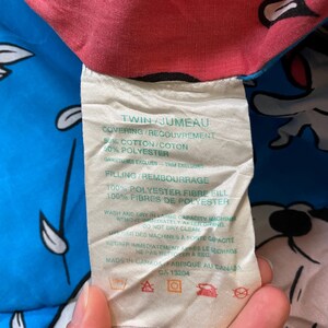 May include: White tag with black text detailing the twin size bedding's materials and care instructions. The tag reads "Twin/Jumeau", "Covering/Recouvrement 50% Cotton/Coton 50% Polyester", "Gartures Excluses Trim Excluded", "Filling/Rembourrage 100% Polyester Fibre Fill 100% Fibres de Polyester", "Wash and dry in large capacity machine. Remove immediately after drying. Do not dry clean.", "Utiliser des machines &agrave; forte capacit&eacute;. Retirer imm&eacute;diatement apr&egrave;s le s&eacute;chage. Ne pas nettoyer &agrave; sec", "Made in Canada/Fabriqu&eacute; au Canada", "CA 13204". The tag has symbols for machine wash, tumble dry, do not dry clean, and do not bleach.