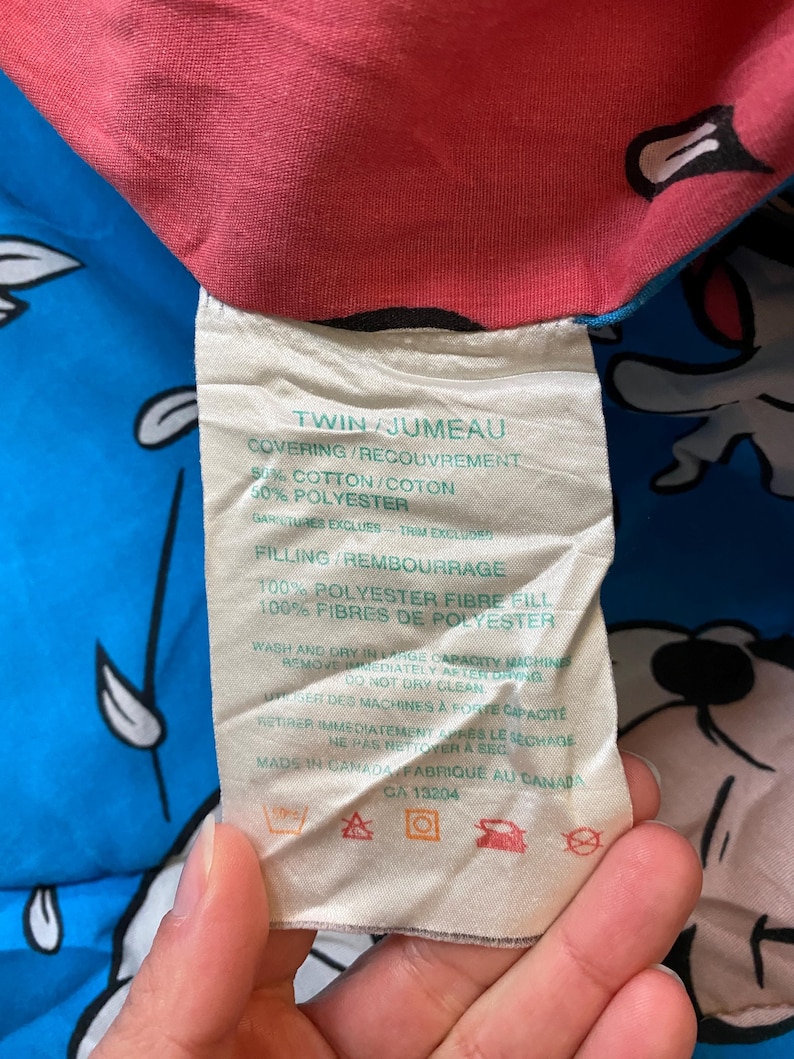 May include: White tag with black text detailing the twin size bedding's materials and care instructions. The tag reads "Twin/Jumeau", "Covering/Recouvrement 50% Cotton/Coton 50% Polyester", "Gartures Excluses Trim Excluded", "Filling/Rembourrage 100% Polyester Fibre Fill 100% Fibres de Polyester", "Wash and dry in large capacity machine. Remove immediately after drying. Do not dry clean.", "Utiliser des machines &agrave; forte capacit&eacute;. Retirer imm&eacute;diatement apr&egrave;s le s&eacute;chage. Ne pas nettoyer &agrave; sec", "Made in Canada/Fabriqu&eacute; au Canada", "CA 13204". The tag has symbols for machine wash, tumble dry, do not dry clean, and do not bleach.