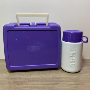 May include: Purple Thermos lunchbox with a white handle and a matching purple and white Thermos food jar.