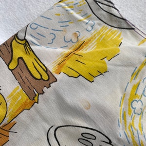 May include: A white fabric with a yellow, brown, and blue cartoon print. The print features a cartoon character wearing yellow gloves and holding a brown stick. The fabric has some brown stains.