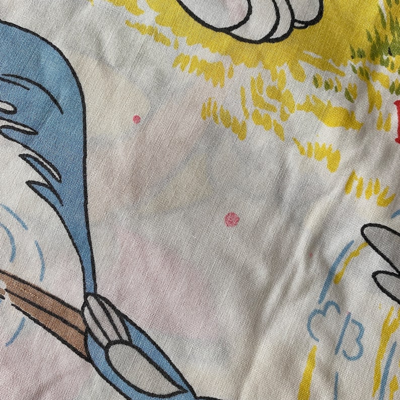 May include: A close-up of a white fabric with a blue and brown cartoon bird design. The bird is flying and has a long tail. The fabric has a yellow and green design in the background.