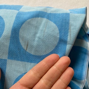 May include: A blue and light blue fabric with a geometric pattern of squares and circles. The fabric has a soft, textured feel.