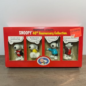 May include: A Snoopy 40th Anniversary Collection set in a red box. The set features four Snoopy figurines with various outfits and speech bubbles. The box has the text "applause. presents" and "40 YEARS OF HAPPINESS."