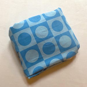 May include: A blue and white fabric with a geometric pattern of circles and squares. The fabric is folded in half.