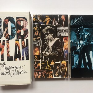 May include: Three VHS tapes featuring Bob Dylan. The first tape is white with black text that reads "Bob Dylan The 30th Anniversary Concert Celebration". The second tape has a collage of photos of Bob Dylan and other musicians. The third tape is black with a photo of Bob Dylan playing guitar on stage.
