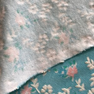 May include: Two pieces of fabric with a floral pattern. The top piece is a light blue fabric with a white and pink floral pattern. The bottom piece is a darker blue fabric with a white and pink floral pattern.