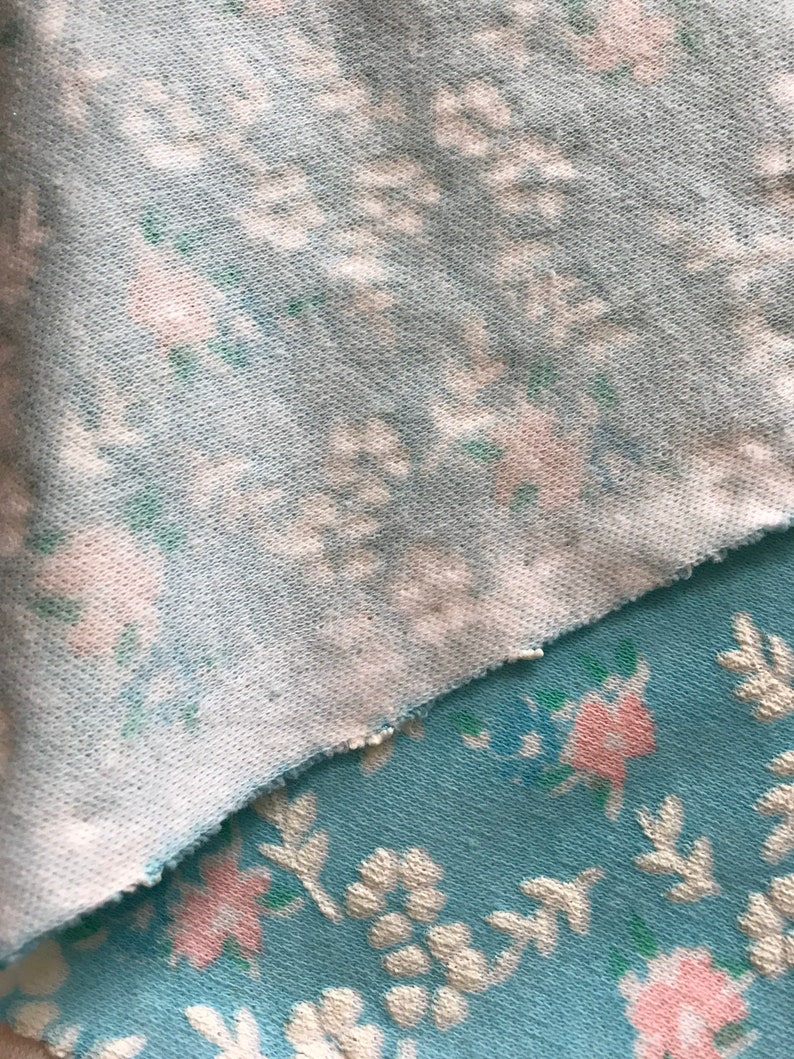 May include: Two pieces of fabric with a floral pattern. The top piece is a light blue fabric with a white and pink floral pattern. The bottom piece is a darker blue fabric with a white and pink floral pattern.