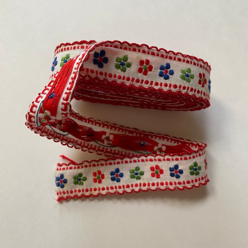 May include: Red and white trim with a scalloped edge and a repeating pattern of blue, green, and red flowers.