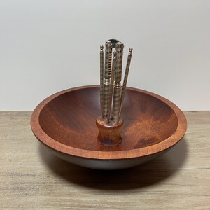 May include: A wooden nut bowl with silver nutcrackers and picks. The bowl is round and a deep brown colour. The nutcrackers and picks are arranged in a small wooden holder in the centre of the bowl.