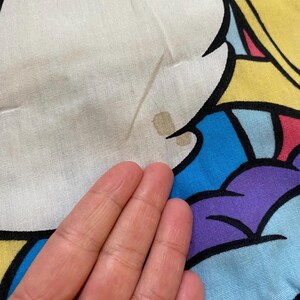 May include: A blue, yellow, purple, and white fabric with a cartoon character on it. The fabric has a brown stain.