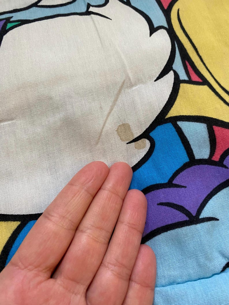 May include: A blue, yellow, purple, and white fabric with a cartoon character on it. The fabric has a brown stain.