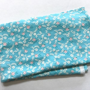 May include: A light blue fabric with a white and pink floral pattern. The fabric is folded in half and has a white border.