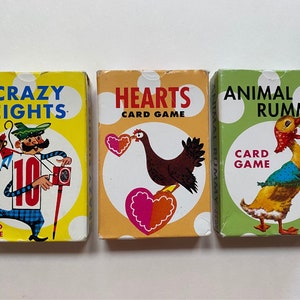 May include: Three card game boxes with colorful illustrations. The first box is yellow with a cartoon man holding a number 10 and the text "Crazy Eights Card Game". The second box is orange with a cartoon chicken holding a heart and the text "Hearts Card Game". The third box is green with a cartoon duck wearing a red bandana and the text "Animal Rummy Card Game".