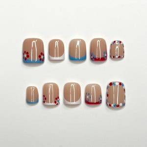 May include: A set of ten artificial nails in various sizes. The nails have a nude base with different designs, including white tips, blue tips, and red and blue floral patterns. The nails are arranged on a white surface.