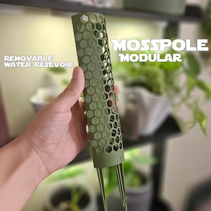 Puede incluir: Tutor de musgo modular verde con diseño de panal. El texto en el poste dice "Moss Pole Modular" y "Removable Water Reservoir". El poste tiene tres patas de soporte.