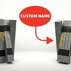 May include: Two gray, rectangular, personalized name blocks with the text "TARS" and "Michael" in gold lettering. A red oval with the text "CUSTOM NAME" is above the blocks, connected by an arrow.
