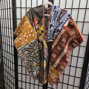 May include: A patchwork kimono-style garment with a variety of patterned fabrics in shades of brown, yellow, blue, and white. The garment is hanging on a pink hanger against a black and white screen.
