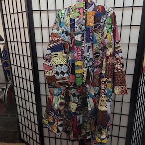 May include: A colorful patchwork jacket with a vibrant mix of patterns and colors, including red, blue, yellow, and green. The jacket is hanging on a metal hanger against a room divider.