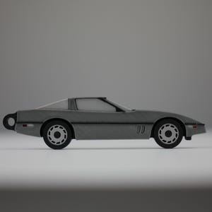 May include: A gray toy car with black wheels and a sleek design. The car has a low profile, a sloped windshield, and a rear spoiler. The wheels have a detailed design. The car is a miniature replica of a classic sports car.