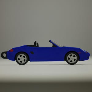 Könnte beinhalten: Ein blaues Spielzeug-Cabrio mit schwarzen Rädern und einem silbernen Windschutzscheibenrahmen. Das Auto hat ein schlankes Design, einen kleinen schwarzen Sitz und einen runden Schlüsselanhänger am Heck.