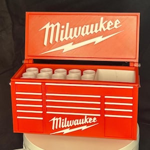 May include: Red Milwaukee toolbox with a white logo and a white lightning bolt. The toolbox has a top compartment with a white divider and a bottom compartment with multiple drawers.
