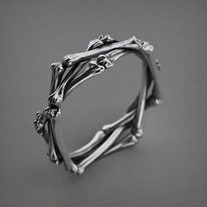 May include: A silver ring with a unique design, featuring a series of interconnected bone-shaped elements. The ring's intricate structure creates a striking visual effect, perfect for those seeking a distinctive accessory. The ring is a statement piece.