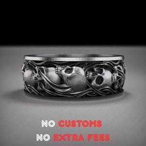 以下が含まれることがあります： スカルと流れるような要素の精巧なデザインが施されたシルバーカラーのリング。リングは幅広のバンドとテクスチャ加工された表面を持っています。「NO CUSTOMS」と「NO EXTRA FEES」の文字が下部に表示されています。