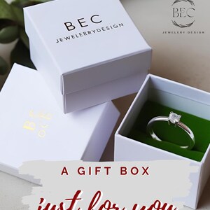 Pu&ograve; includere: Scatole regalo bianche impilate con il testo "BEC JEWELRY DESIGN". Una scatola &egrave; aperta, rivelando un anello d'argento con una gemma quadrata su un inserto di velluto verde. Il testo "A GIFT BOX just for you" &egrave; visualizzato.