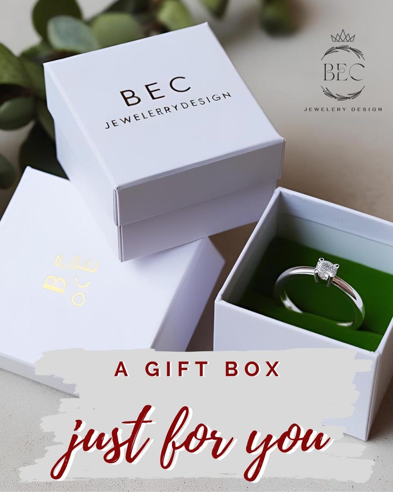 Pu&ograve; includere: Scatole regalo bianche impilate con il testo "BEC JEWELRY DESIGN". Una scatola &egrave; aperta, rivelando un anello d'argento con una gemma quadrata su un inserto di velluto verde. Il testo "A GIFT BOX just for you" &egrave; visualizzato.