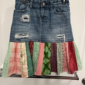 May include: A denim skirt with a patchwork ruffle hem. The skirt is blue with distressed details and the ruffle is made of various colorful fabrics with floral and plaid patterns.