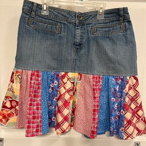 May include: A denim skirt with a patchwork ruffle hem. The ruffle is made of different fabrics in shades of red, blue, and white with floral and geometric patterns.
