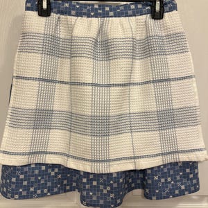 May include: A white and blue checkered skirt with a blue and white patterned ruffle at the bottom.