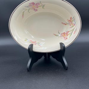 May include: An oval-shaped, off-white serving bowl with a brown rim and floral design. The bowl is supported by a black stand. The floral pattern features pink and purple flowers with green leaves.