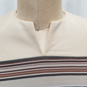 May include: A beige shirt with a V-neck and horizontal stripes in brown, black, and white.