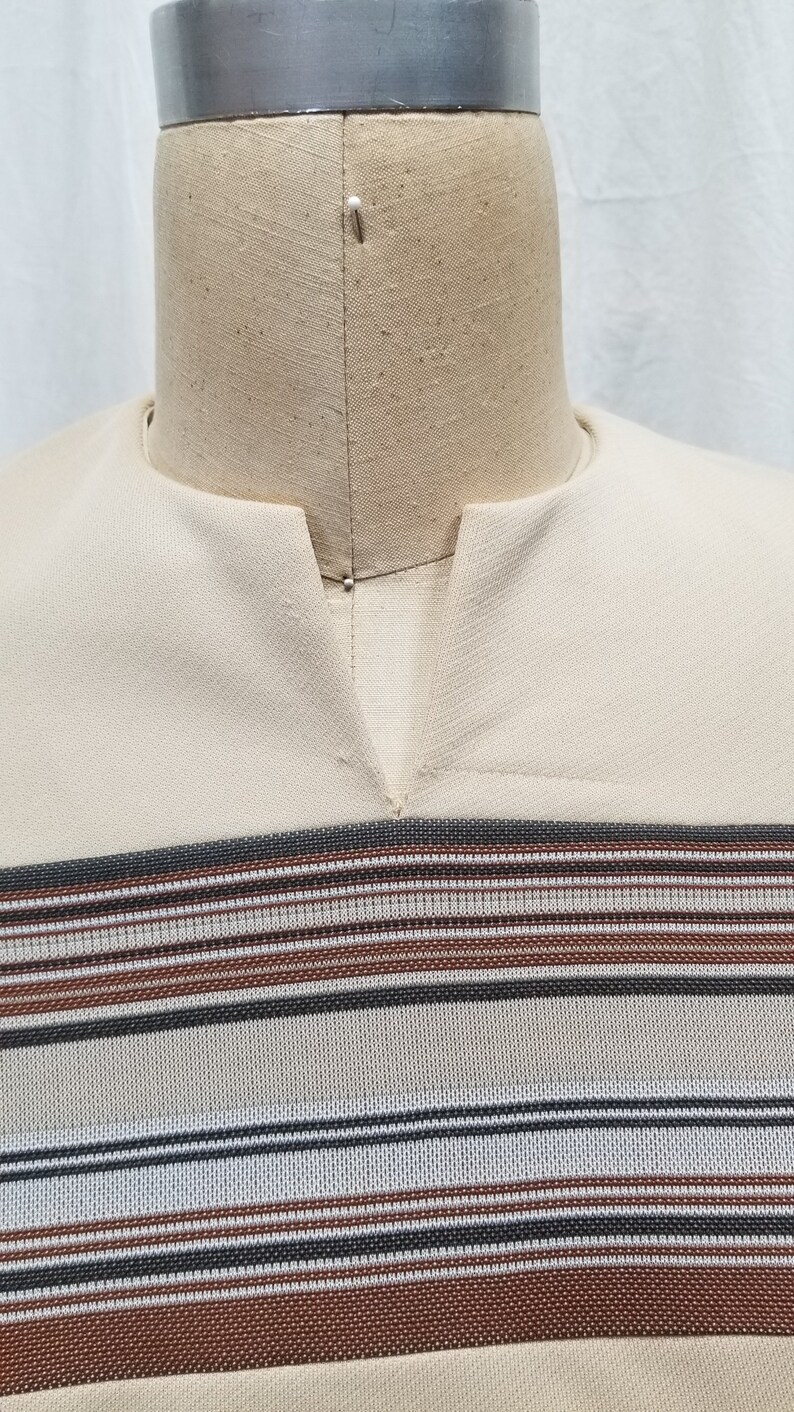 May include: A beige shirt with a V-neck and horizontal stripes in brown, black, and white.