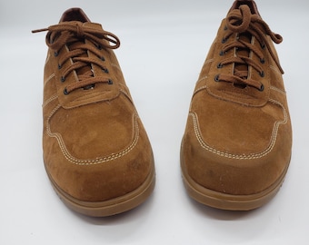 May include: A pair of brown suede sneakers with matching laces. The shoes have a rounded toe and a stitched design along the seams. The soles are a darker shade of brown.