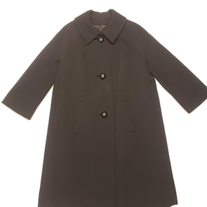 May include: A dark brown coat with a classic design. The coat features a collar, three black buttons, and two front pockets. The sleeves are three-quarter length, and the coat has a slightly flared shape.