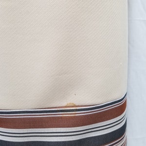 May include: A cream-colored dress with a brown, black, and white striped band at the hem.