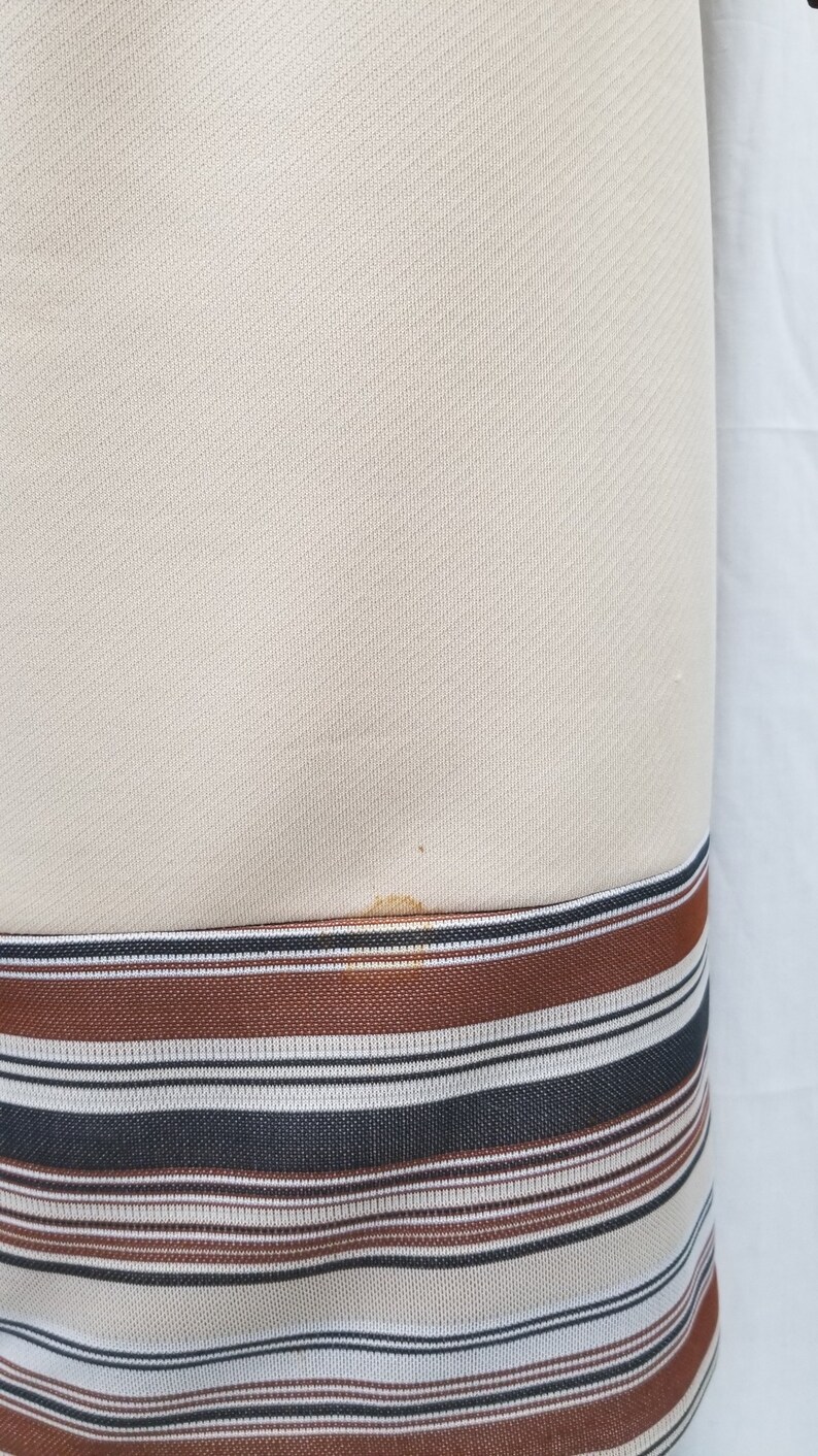 May include: A cream-colored dress with a brown, black, and white striped band at the hem.