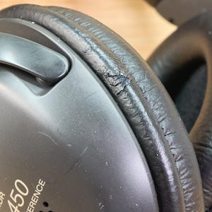 May include: Close-up of black headphones with visible wear and tear on the ear cushion. The text "CD450 DIGITAL REFERENCE" is printed on the side of the headphones. The ear cushion shows signs of cracking and peeling.
