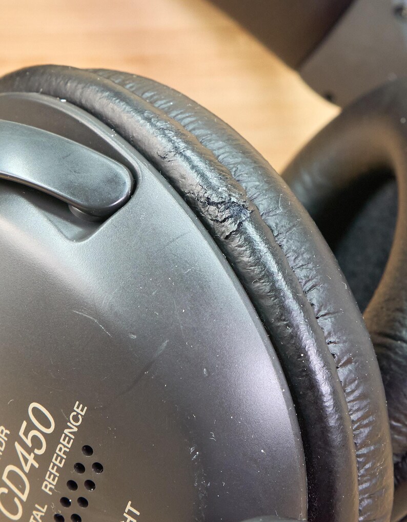 May include: Close-up of black headphones with visible wear and tear on the ear cushion. The text "CD450 DIGITAL REFERENCE" is printed on the side of the headphones. The ear cushion shows signs of cracking and peeling.