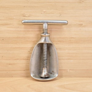 May include: A vintage ice cream scoop with a silver finish. The scoop has a T-shaped handle and a spring mechanism inside. The scoop is made of metal and is designed to scoop ice cream. The scoop is approximately 18 cm long.