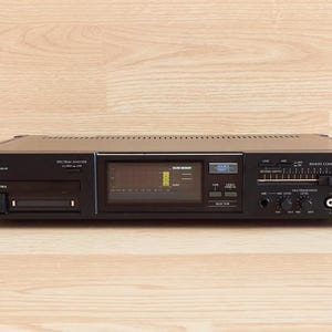 May include: A black Sansui SE-88 stereo graphic equalizer featuring a central spectrum monitor display, a remote control sensor, multiple slider controls for frequency adjustment, a microphone input, and RCA audio input and output jacks.