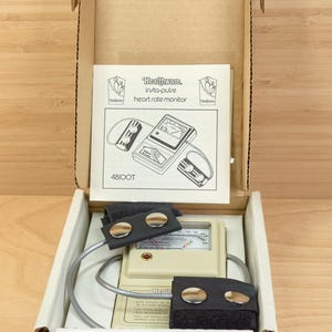 May include: A vintage Healthware insta-pulse heart rate monitor in its original cardboard box. The device is beige with a dial and black sensor pads. The box also contains a manual with the product name and model number 48100T.
