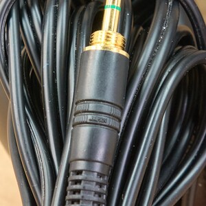 May include: Close-up of a black audio cable with a gold-colored 3.5mm connector. The connector has green accents and the word "JAPAN" is printed on the black plastic casing. The cable is coiled and appears to be new.
