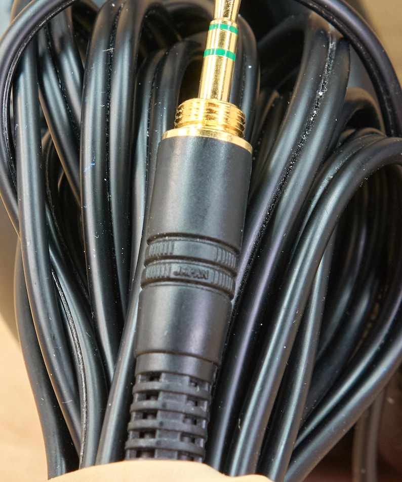 May include: Close-up of a black audio cable with a gold-colored 3.5mm connector. The connector has green accents and the word "JAPAN" is printed on the black plastic casing. The cable is coiled and appears to be new.