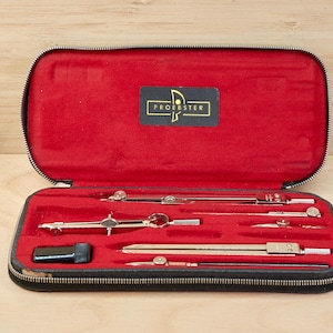 May include: A black zippered case with a red velvet interior, containing several silver drafting tools. The case has a gold label that reads "PROEESTER". The tools include compasses and dividers, used for technical drawing and geometry.